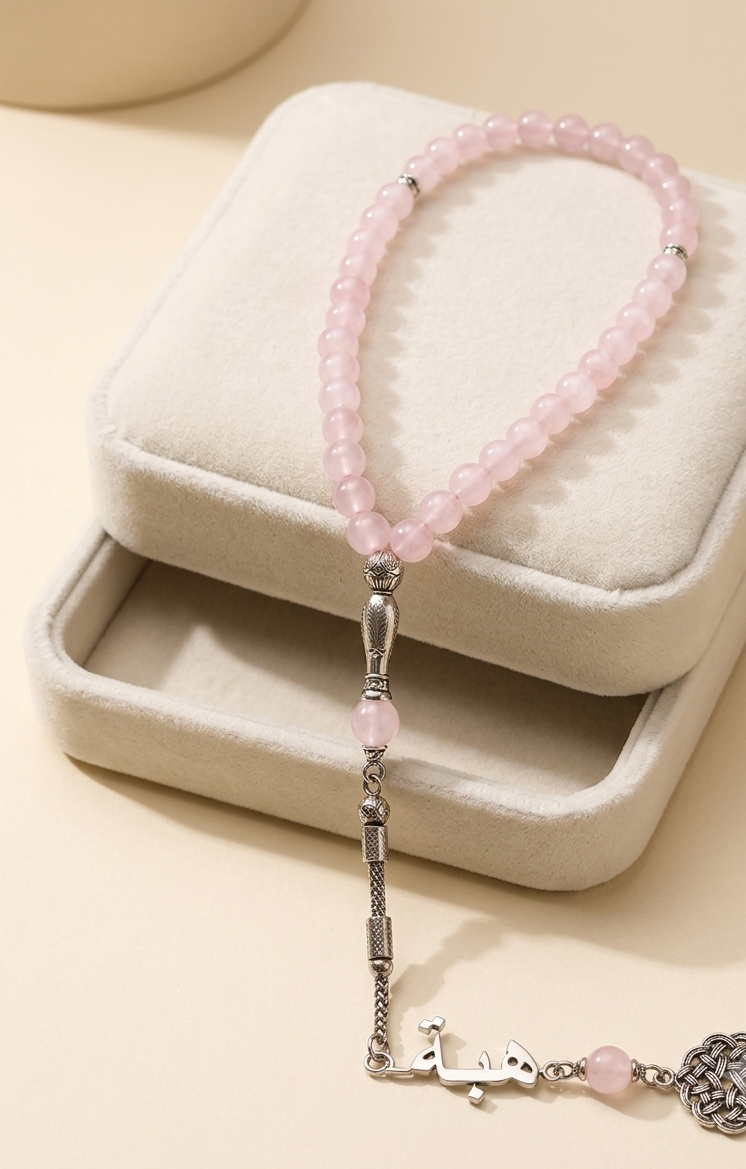 A pink beaded bracelet with silver-toned metal details and a dangling charm, displayed on a cream-colored jewelry box.