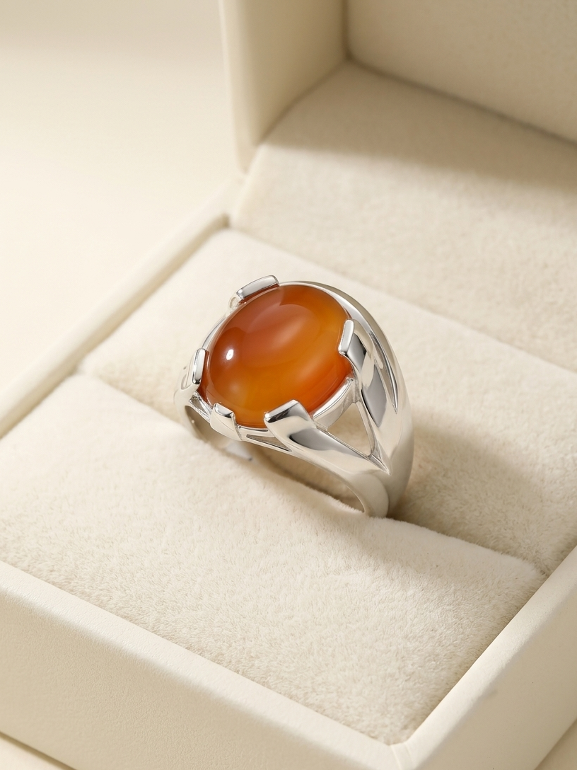 A silver ring with a large oval amber-orange cabochon gemstone, displayed inside a cream-colored jewelry box.