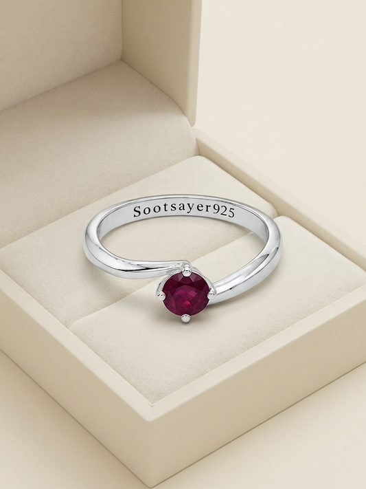 A sterling silver ring with a round deep red gemstone, displayed inside a cream-colored jewelry box. The inside of the band is engraved with 'Sootsayer925'.