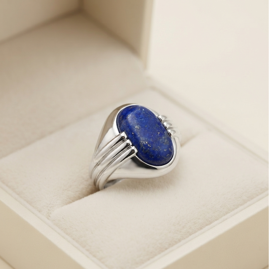 A silver ring with a large oval blue lapis lazuli stone, displayed inside a cream-colored jewelry box.