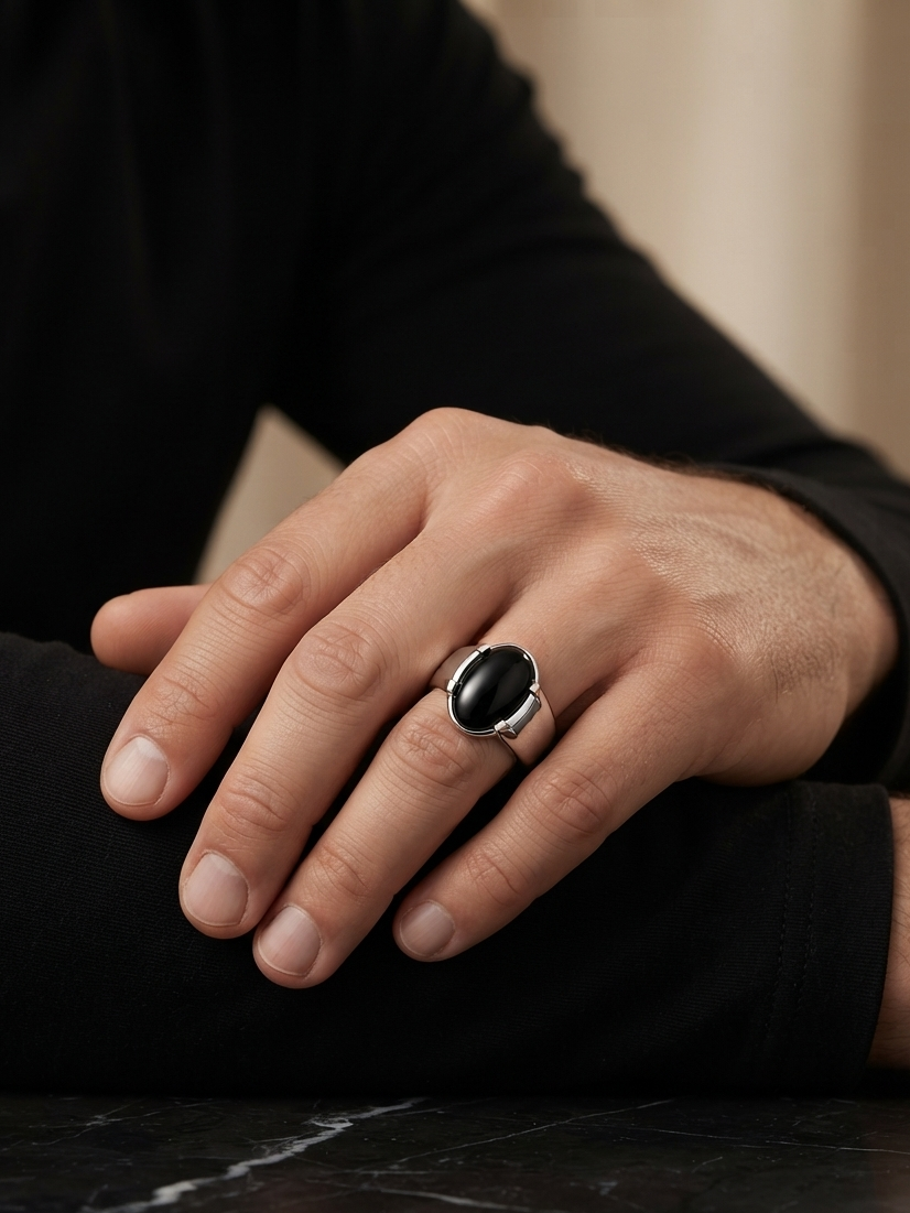 A close-up of a person's hand resting on their knee, wearing a silver-toned ring with a large, smooth black oval cabochon stone.