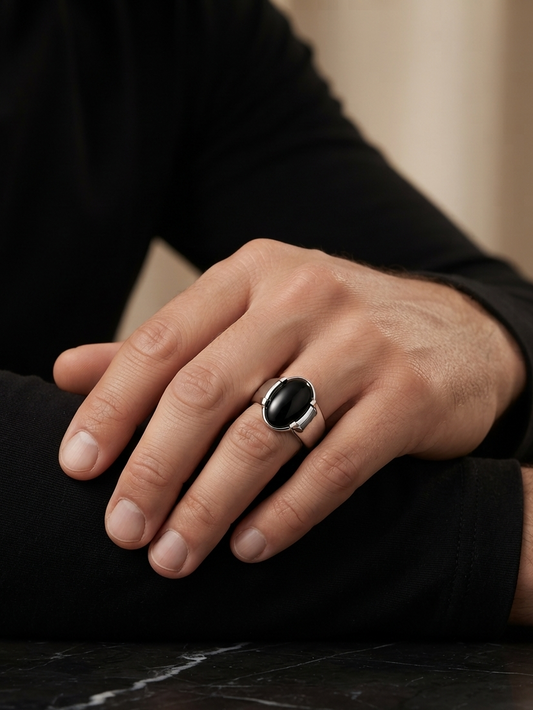 A close-up of a person's hand resting on their knee, wearing a silver-toned ring with a large, smooth black oval cabochon stone.