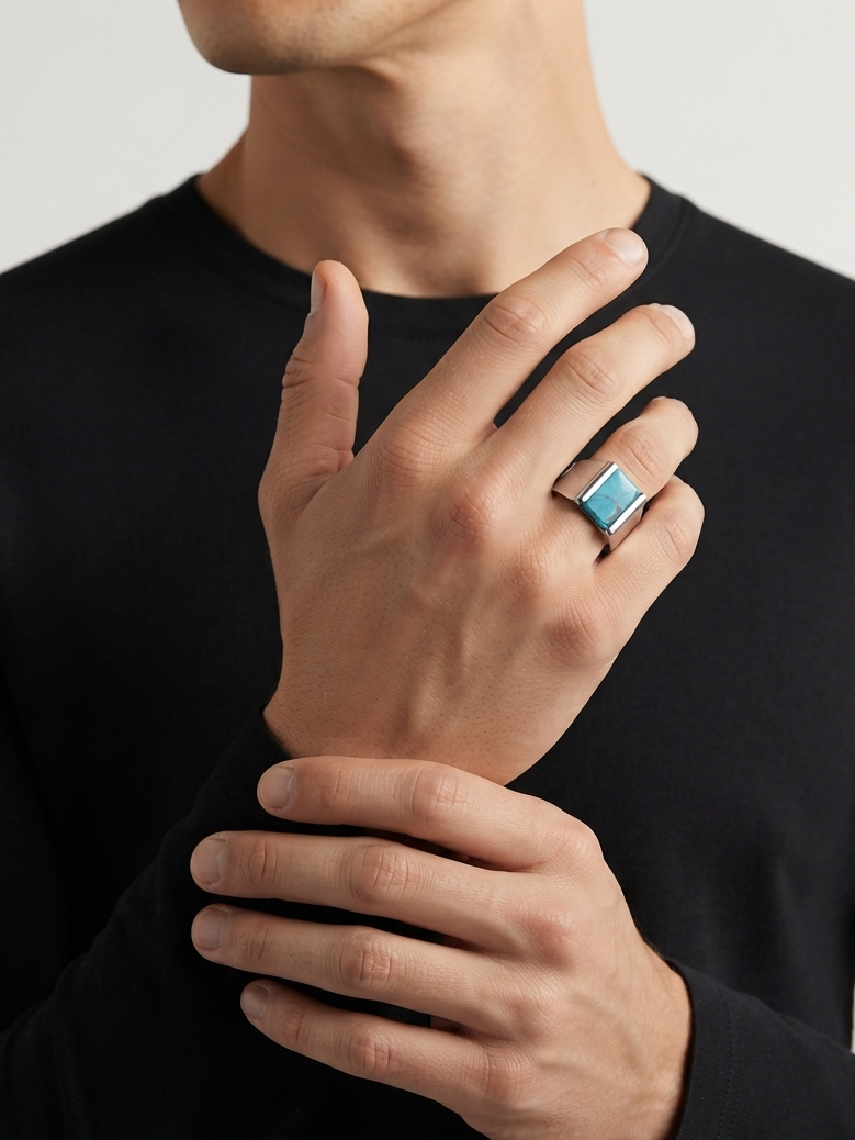 A close-up of a man wearing a black long-sleeve shirt, showcasing a silver-toned ring with a square turquoise blue stone on his ring finger.