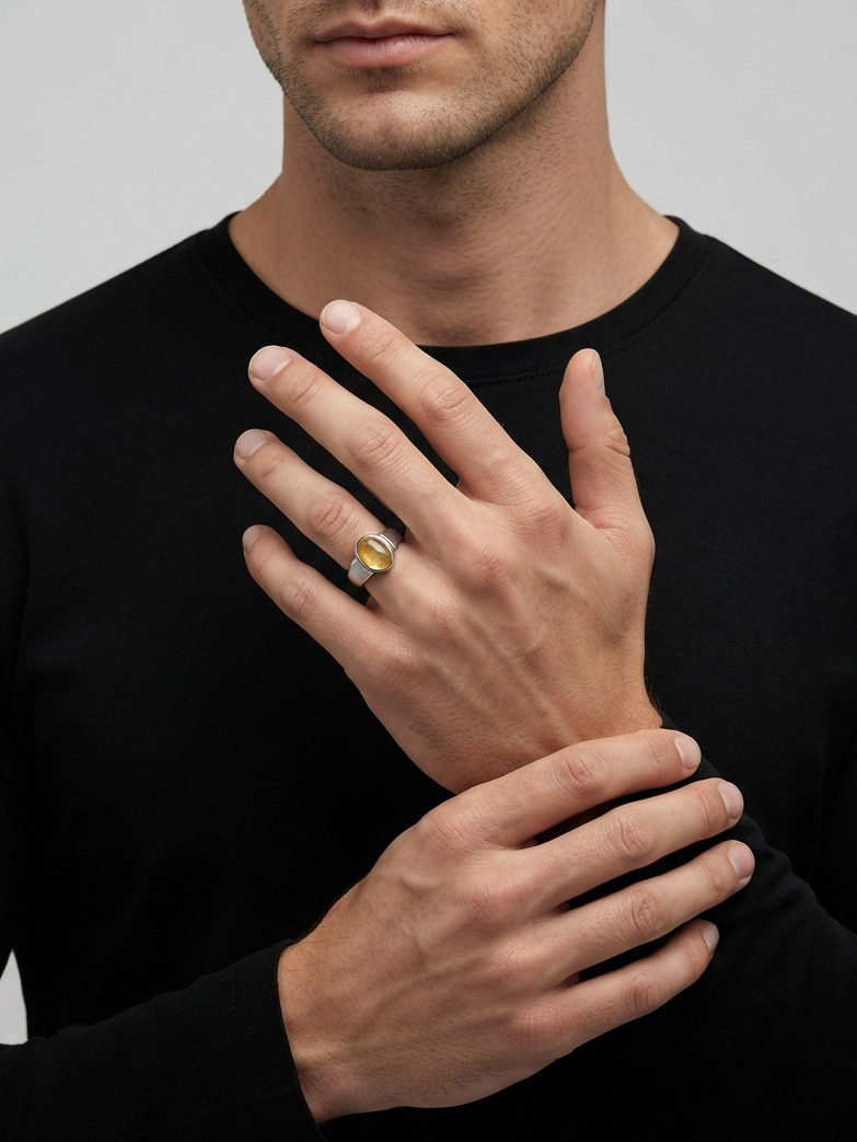 A close-up of a man wearing a black long-sleeve shirt, showcasing a silver ring with a small oval yellow gemstone on his ring finger.