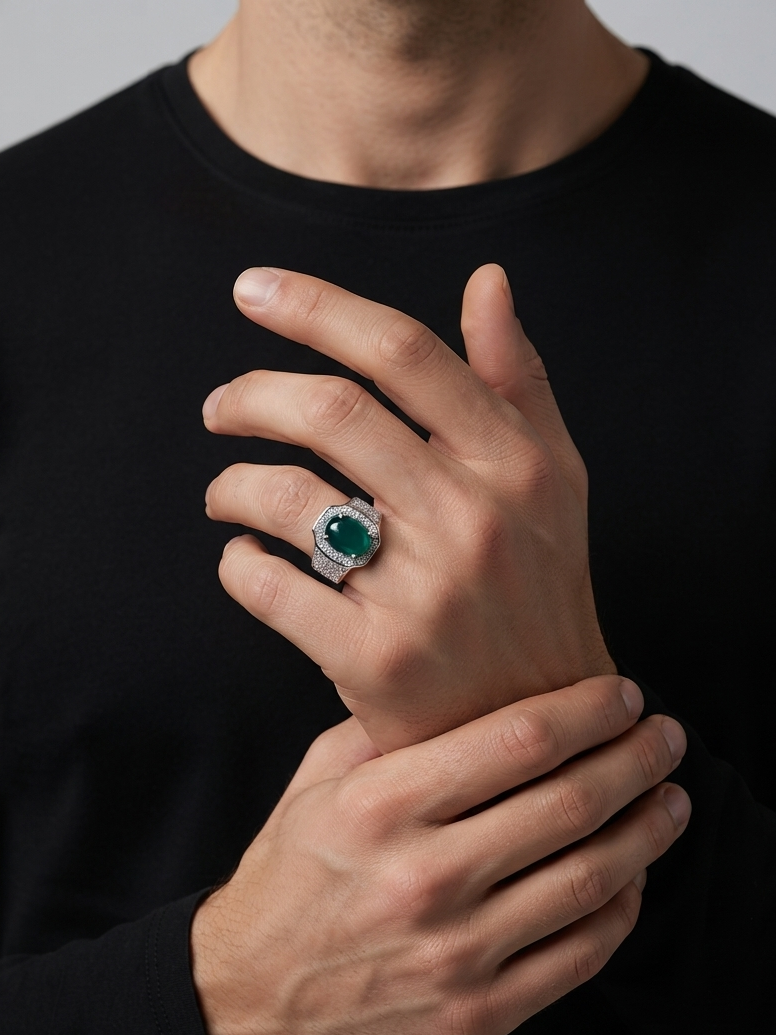 A close-up of a man wearing a black long-sleeve shirt, showcasing a silver-toned ring with a round green emerald-cut center stone on his ring finger.