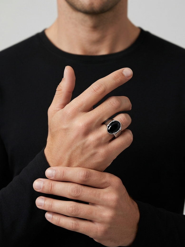 A close-up of a man wearing a black long-sleeve shirt and adjusting his wrist with one hand while wearing a silver-toned ring with a large oval black stone on the other hand.