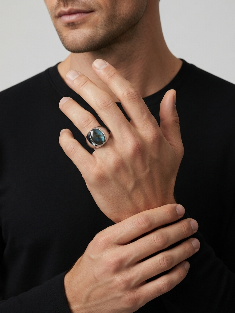 A close-up of a man wearing a black long-sleeve shirt, showcasing a silver ring with a round, dark blue-green stone on his ring finger.