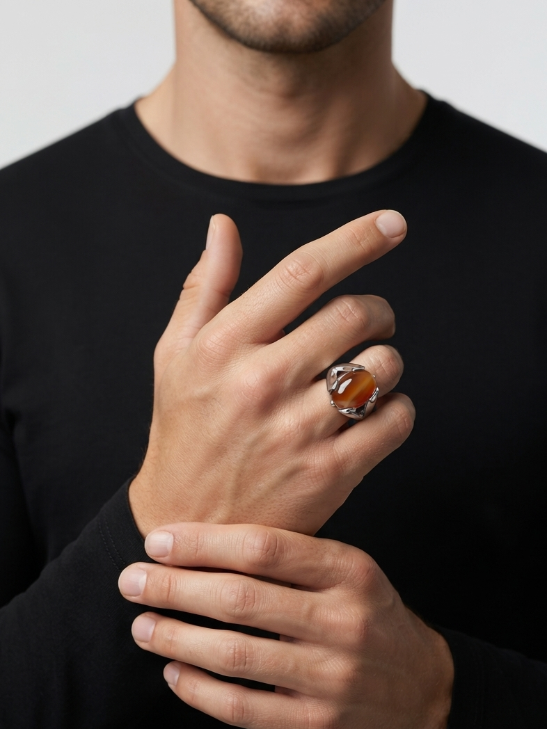 A close-up of a man wearing a black long-sleeve shirt, showcasing a silver ring with a polished oval amber gemstone on his ring finger against a light gray background.