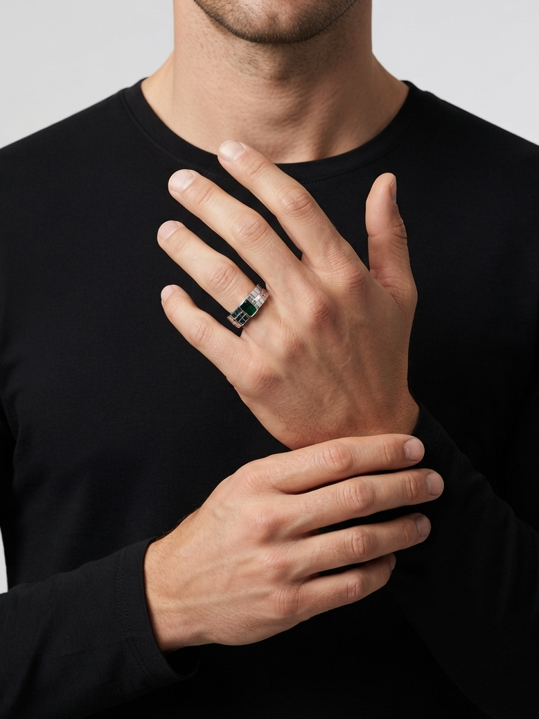 A close-up of a man wearing a black long-sleeve shirt, showcasing a silver ring with a green rectangular inlay on his ring finger against a light gray background.