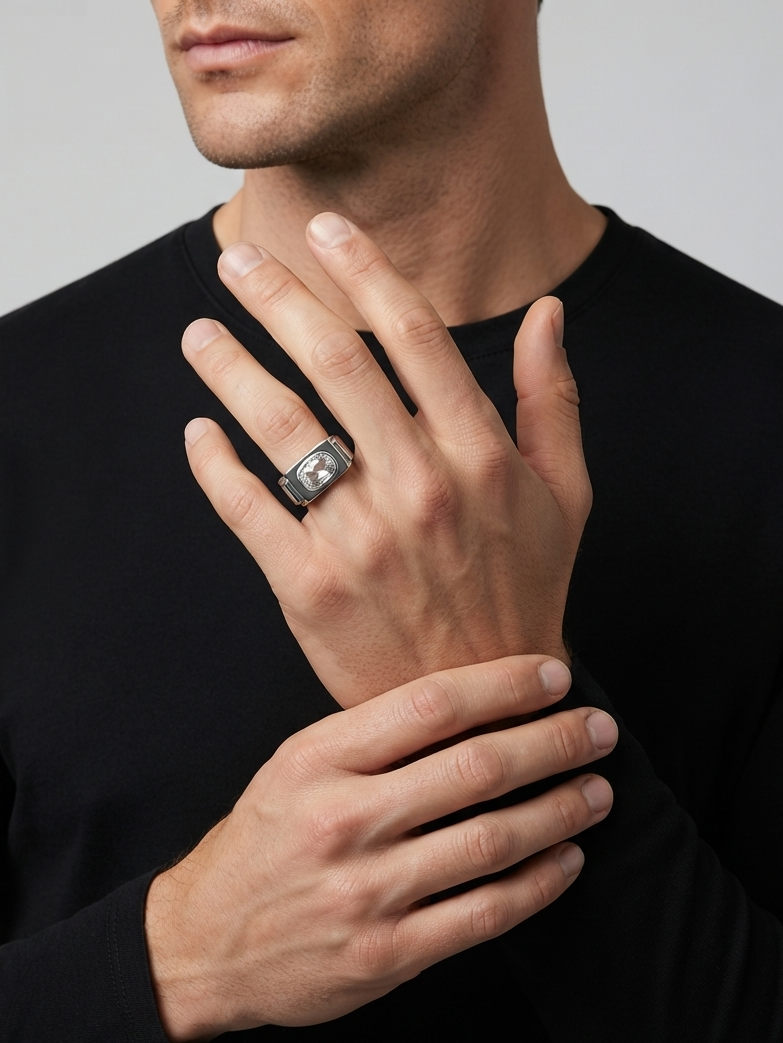 A close-up of a man wearing a silver-toned ring with a square-cut clear gemstone on his ring finger, wearing a black long-sleeve shirt against a light gray background.