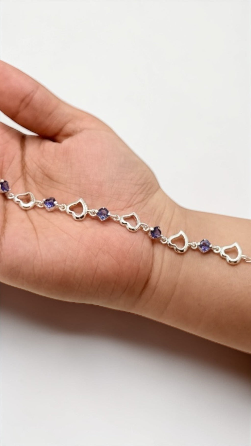 Silver bracelet with heart-shaped links and purple beads on a hand against a white background