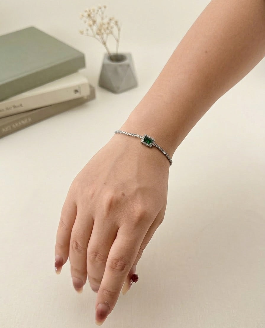 Hand wearing a bracelet with a green gemstone on a neutral background