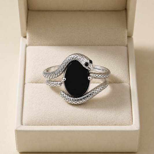 A silver snake ring with a black onyx oval center stone, displayed inside a beige jewelry box.