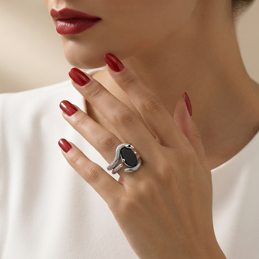 A close-up lifestyle shot of a woman wearing a silver ring with a black oval stone, shown on her hand as she wears a white sleeveless top and has dark red manicured nails.