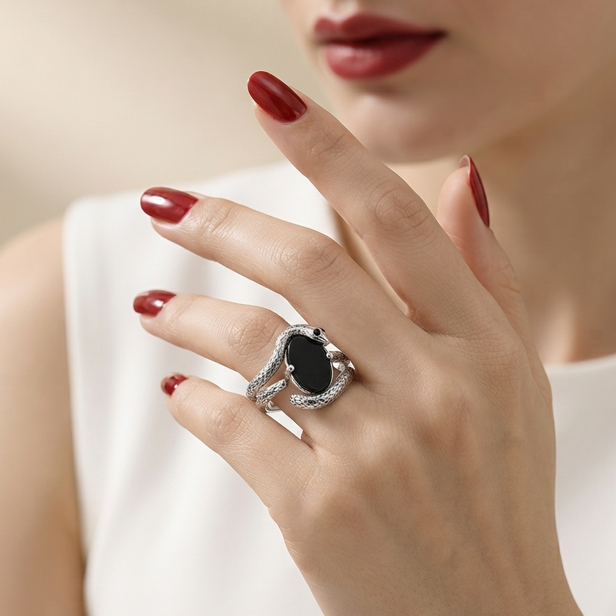 A close-up lifestyle shot of a woman's hand wearing a silver ring with a large oval black gemstone, set against a soft beige background.