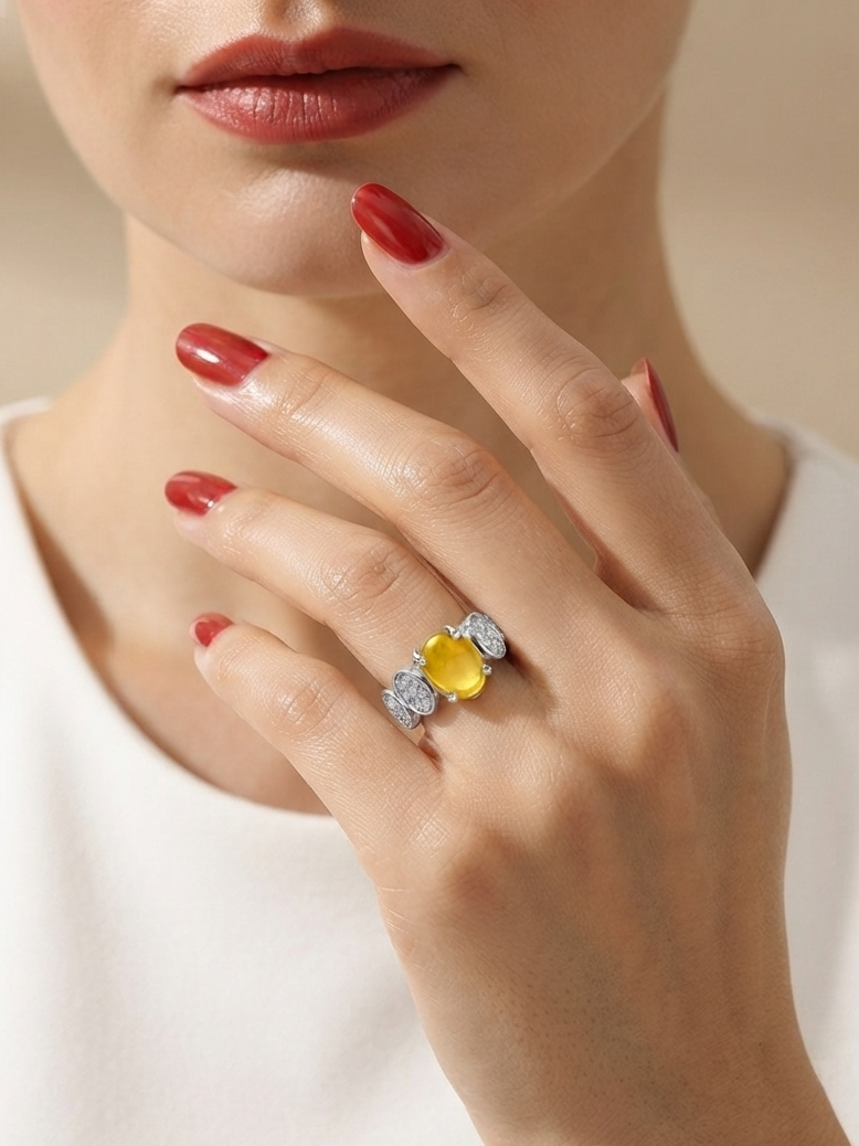 A close-up lifestyle shot of a model wearing a yellow flower-shaped ring with silver-toned pavé accents on her finger, paired with red nail polish and a white top.