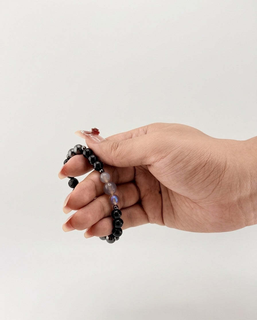 Hand holding a black beaded bracelet against a white background