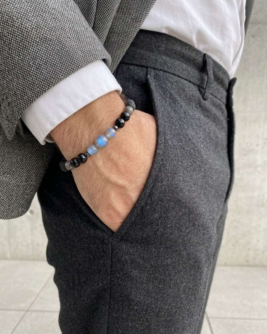 Person wearing a gray suit with a white shirt and black pants, holding a black beaded bracelet.