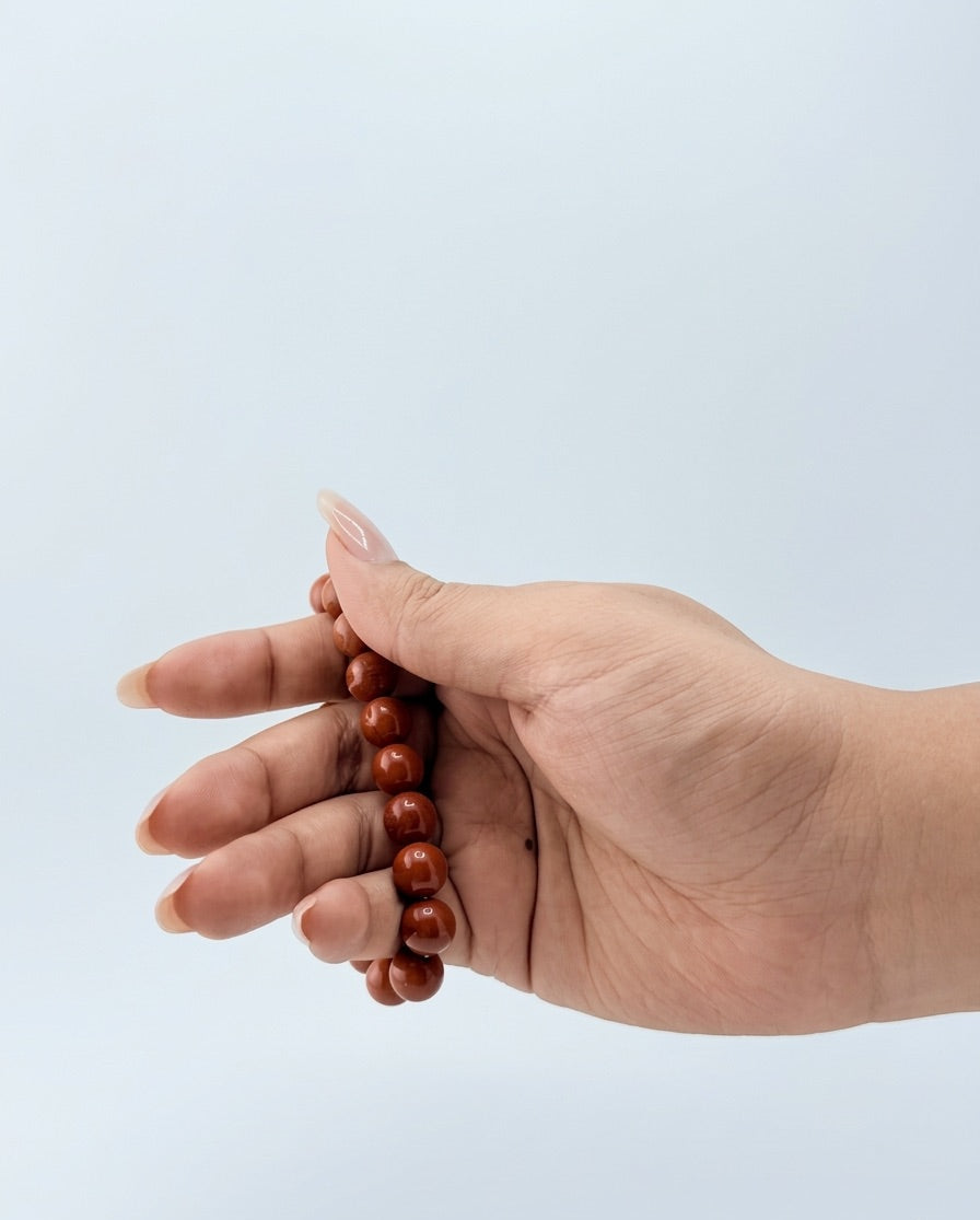 Hand holding a red beaded bracelet against a light blue background