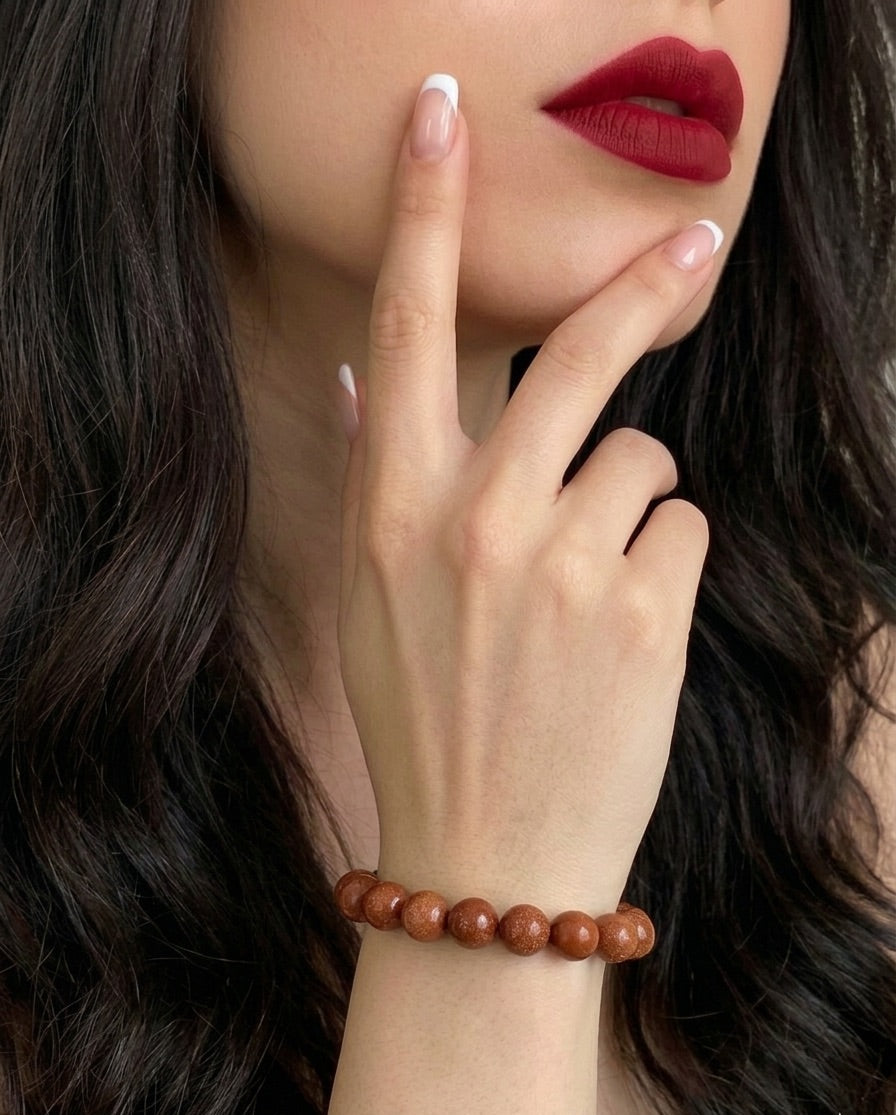 Close-up of a woman's hand wearing a brown beaded bracelet with red lipstick and dark hair.
