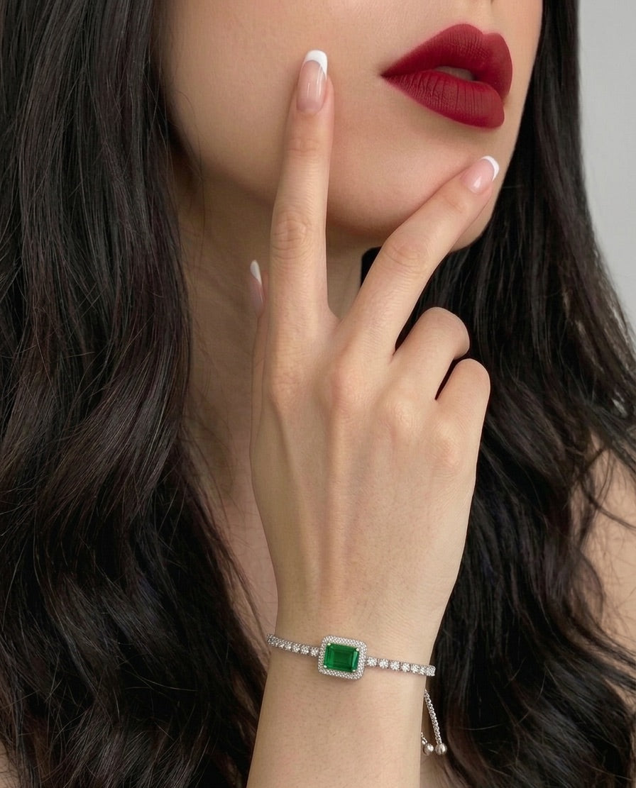 Close-up of a hand wearing a bracelet with a green gemstone, against a neutral background.