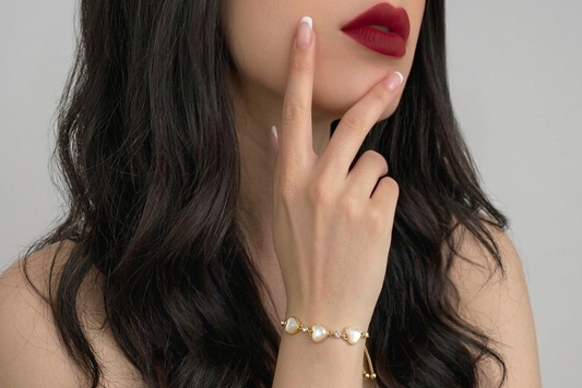 Woman wearing a gold bracelet with heart-shaped charms on a neutral background