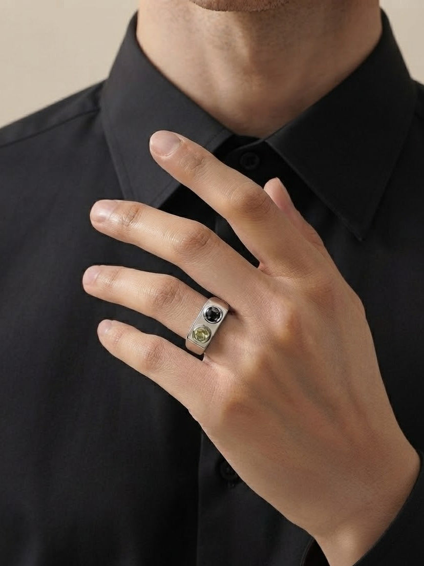 A close-up of a person's hand wearing a silver ring with a black and green stone set against a black shirt.