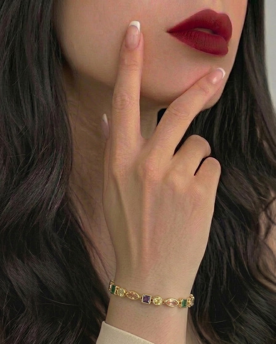 Close-up of a hand wearing a gold bracelet with gemstones, touching the face.