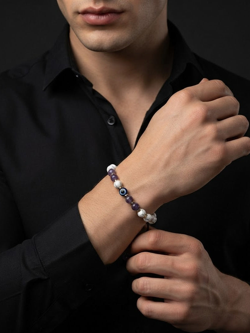 A close-up of a man wearing a beaded bracelet on his wrist, adjusting his black dress shirt. The bracelet features white pearl-like beads, purple beads, and evil eye charms.