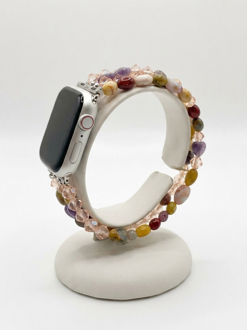 A multicolor beaded stretch watch band displayed on a white stand, holding a silver smartwatch. The beads feature a mix of pink, yellow, purple, green, and orange tones.