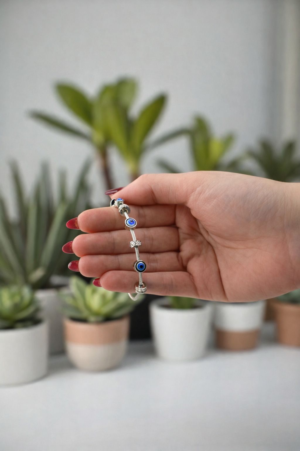 Hand holding a silver bracelet with blue stones in front of potted plants