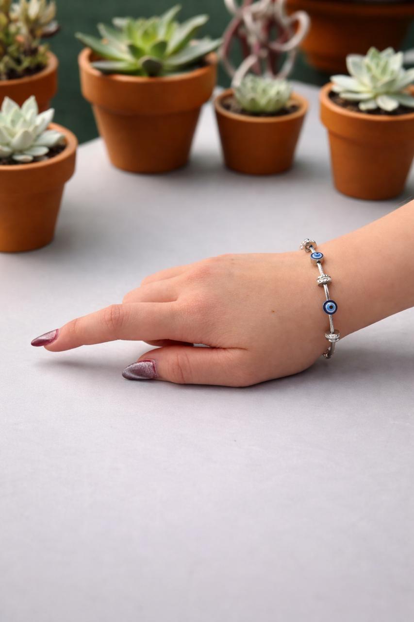 Hand wearing a bracelet with potted plants in the background