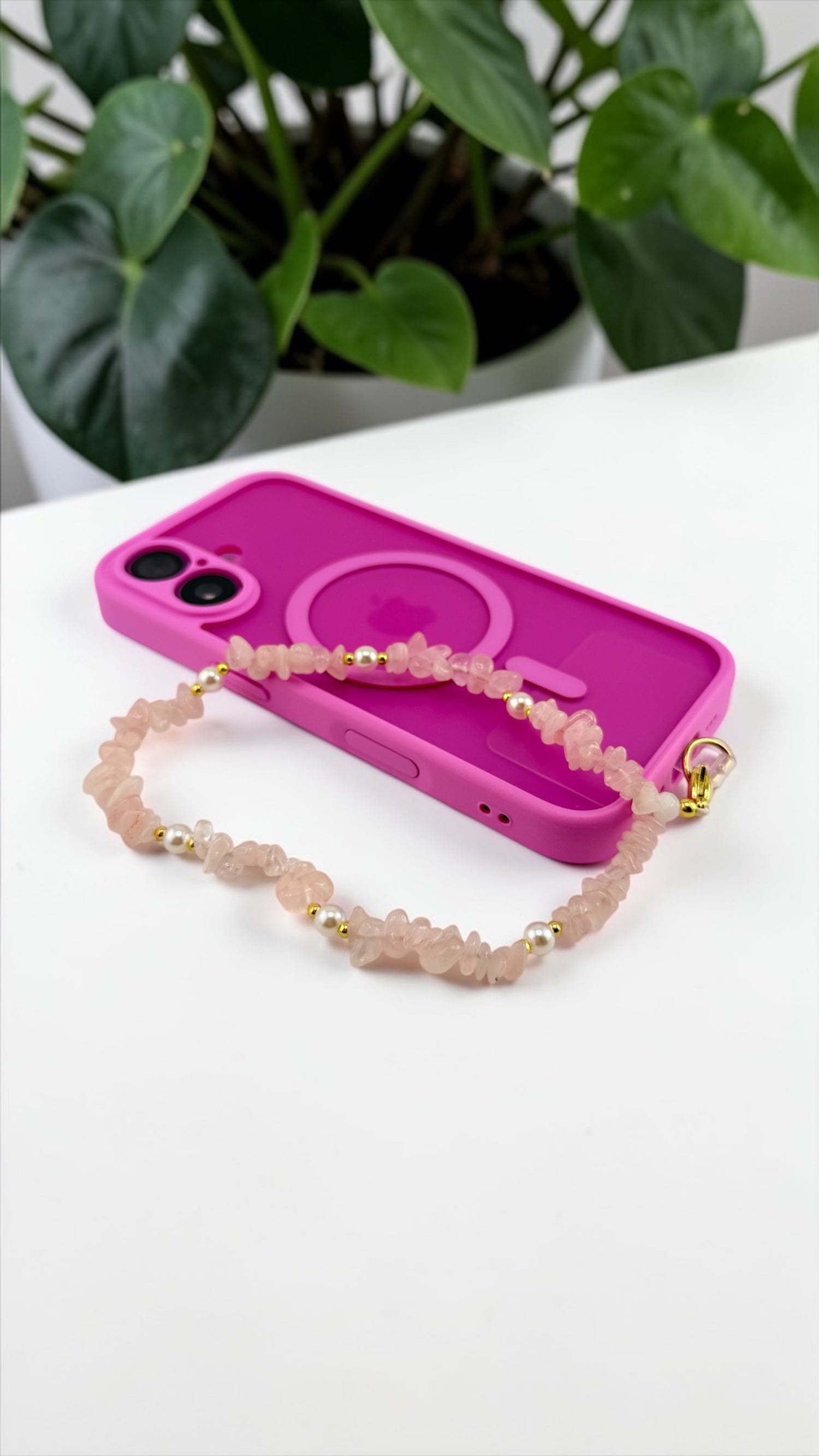Pink phone case with a beaded chain on a white surface with green plants in the background