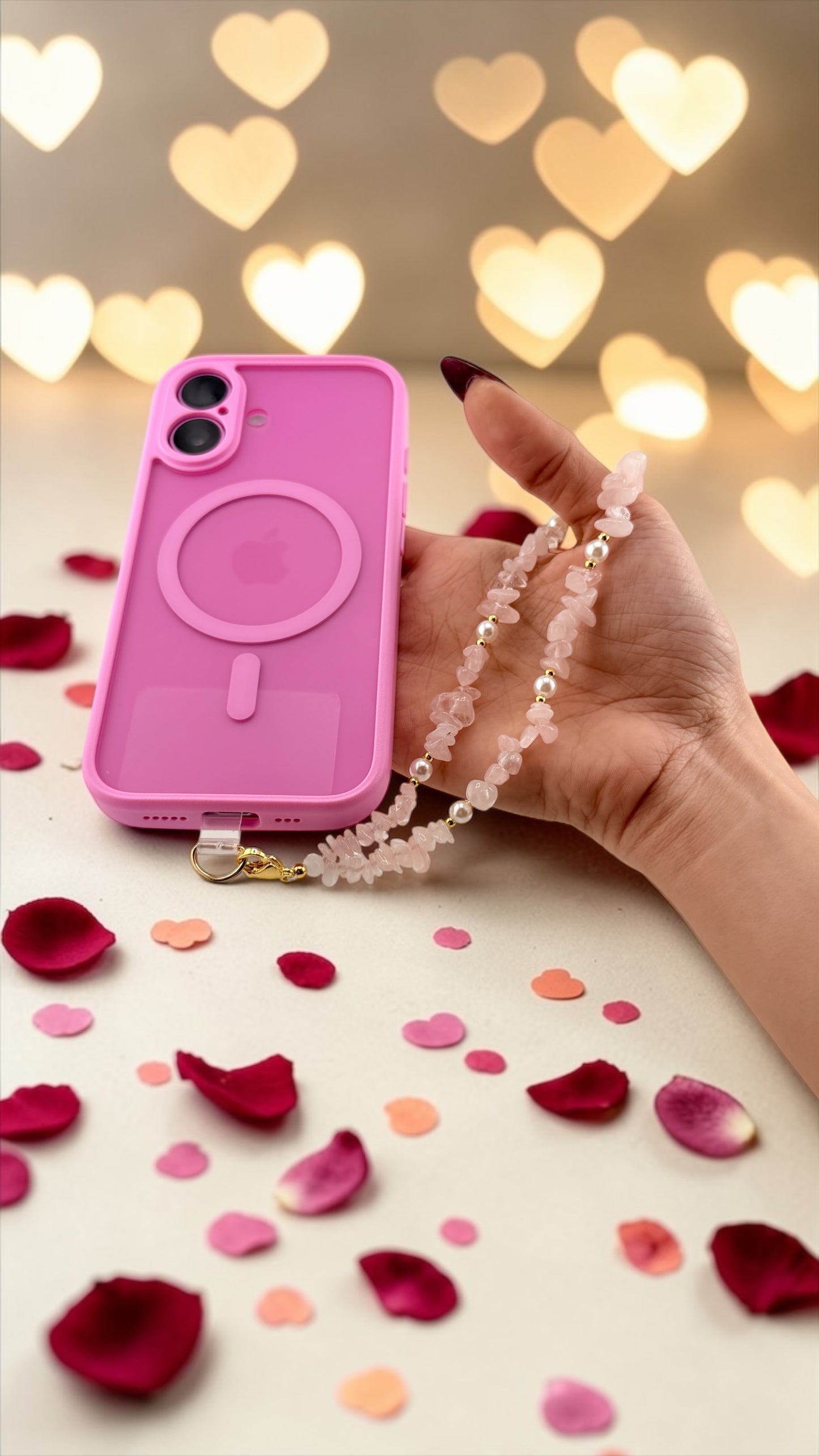 Hand holding a pink phone case with a strap against a heart-shaped light bokeh background