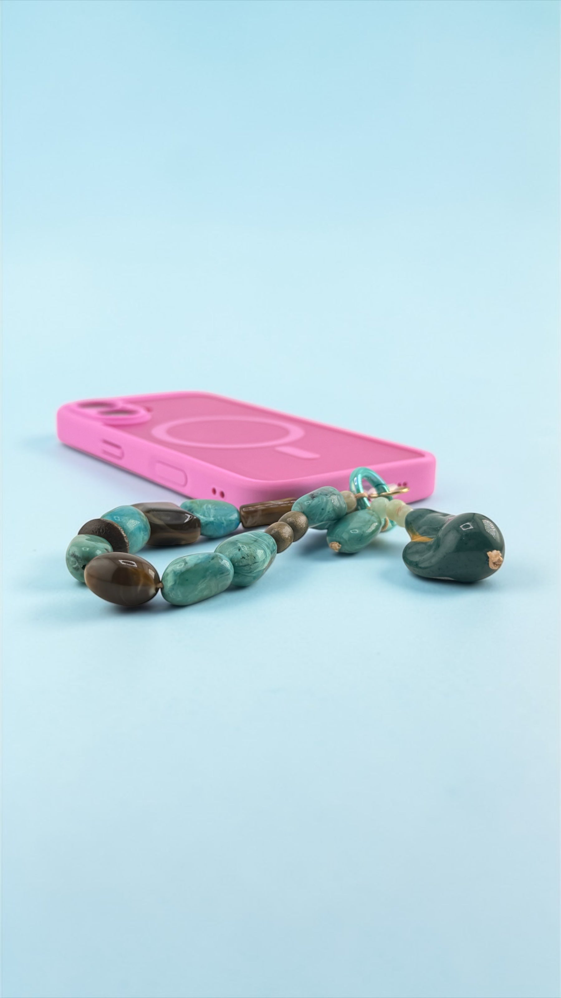 Turquoise and brown beaded necklace on a pink phone case against a light blue background