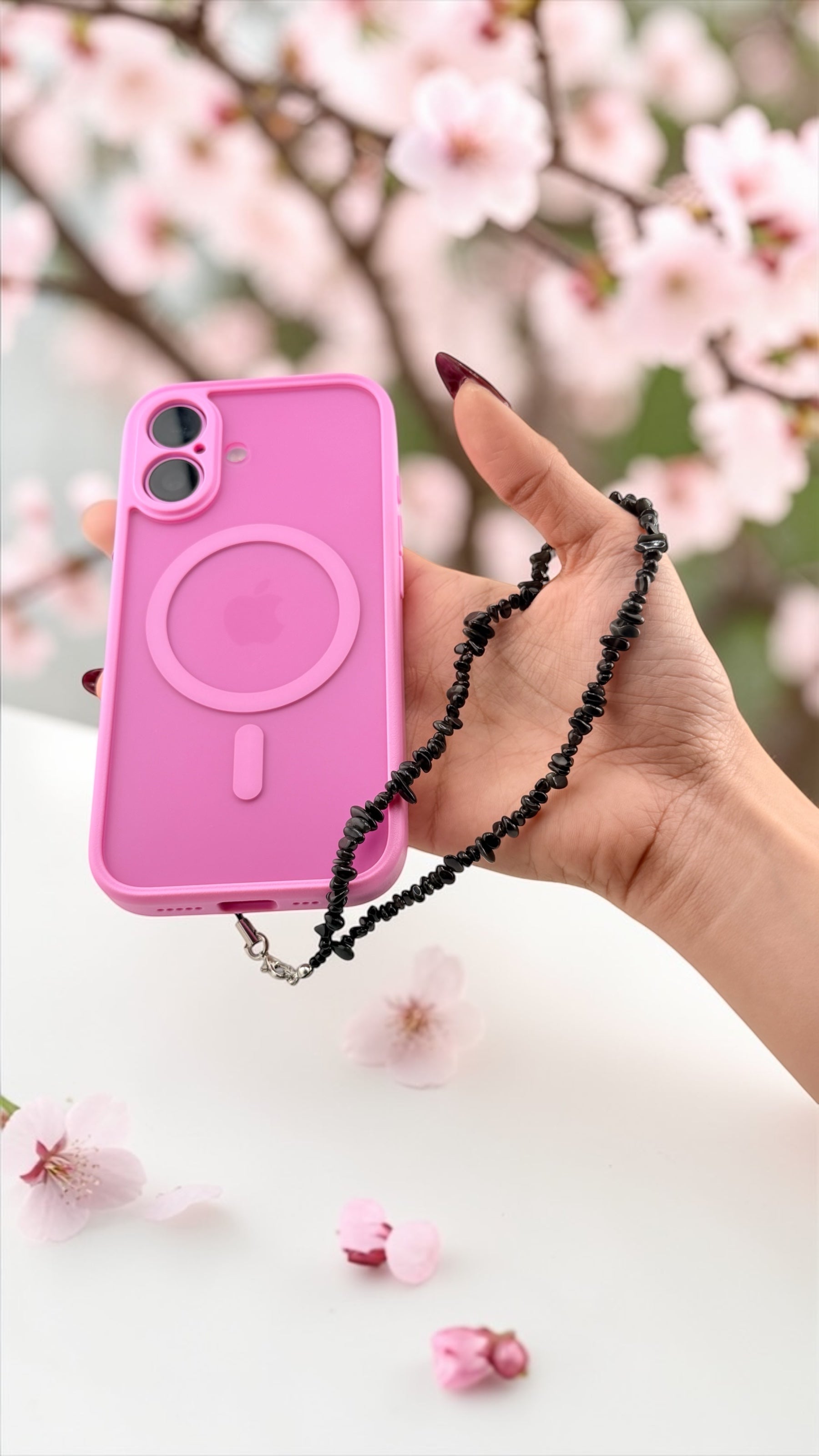 Pink phone case with a black chain held by a hand in front of cherry blossoms