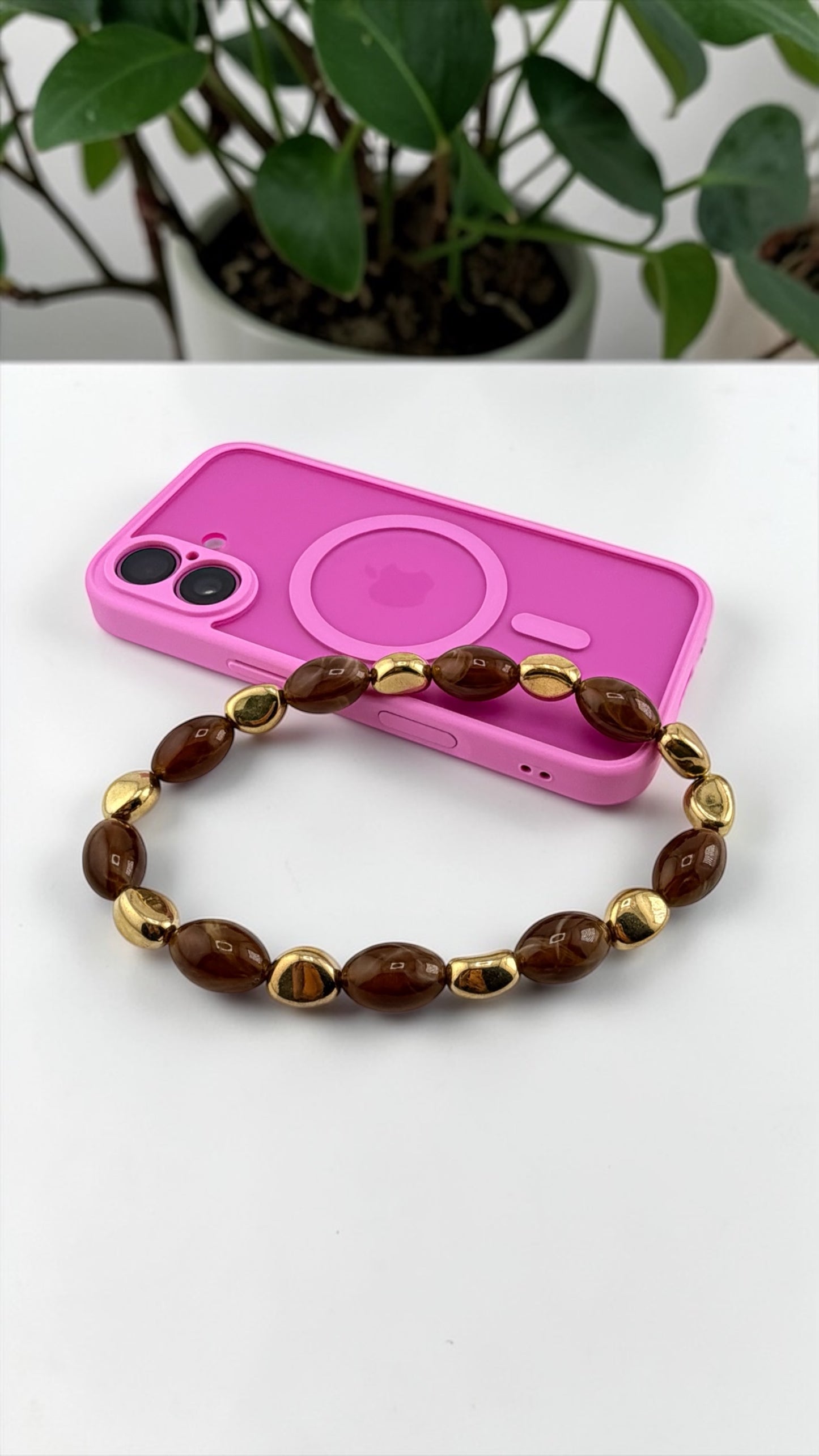 Brown beaded bracelet on a pink phone case with a plant in the background
