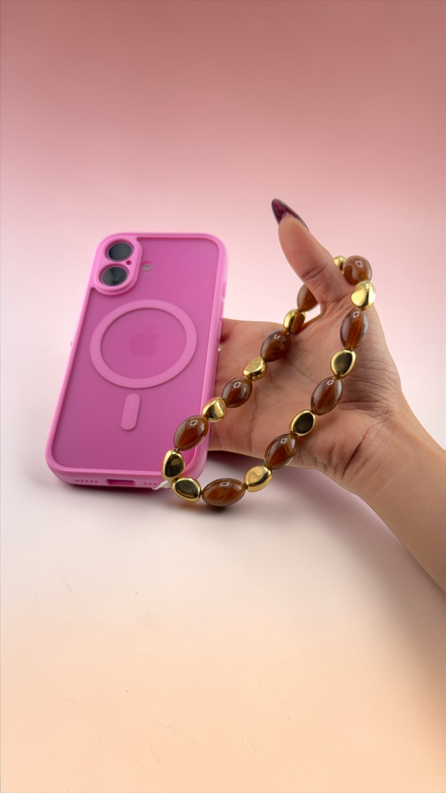 Hand holding a pink phone case with a gold chain against a gradient background