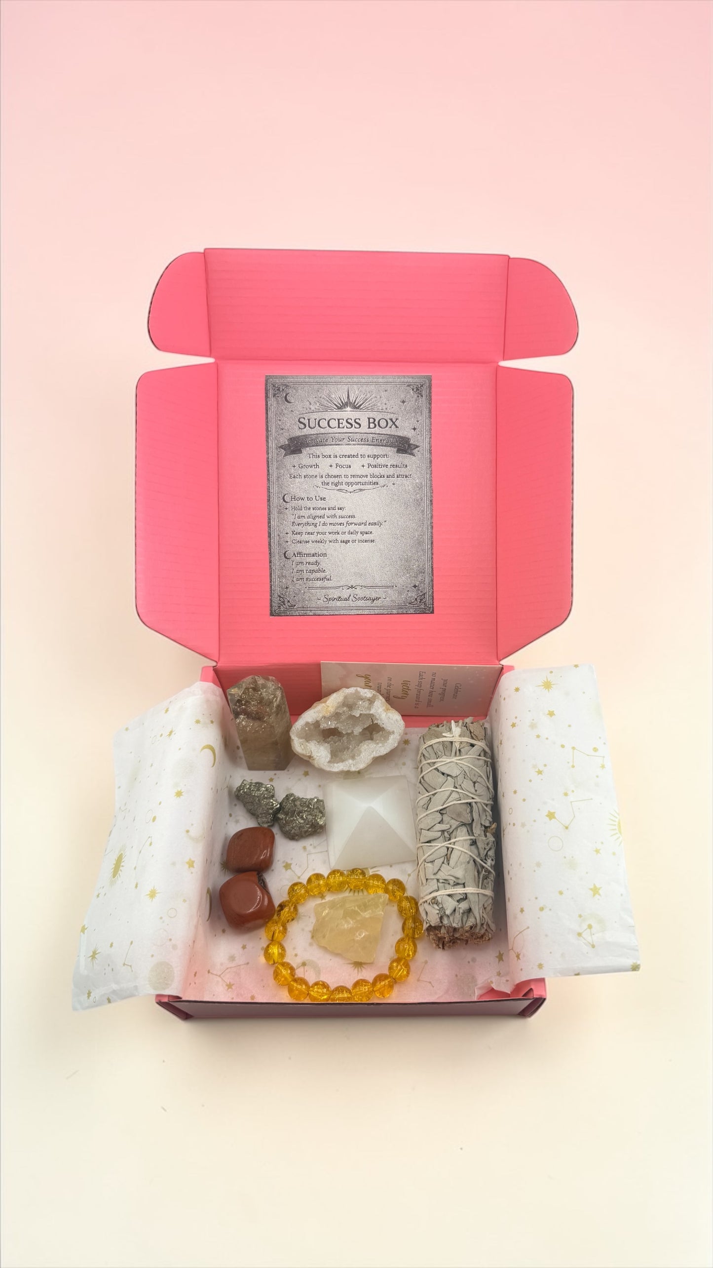 Open pink box containing crystals and a card on a light pink background