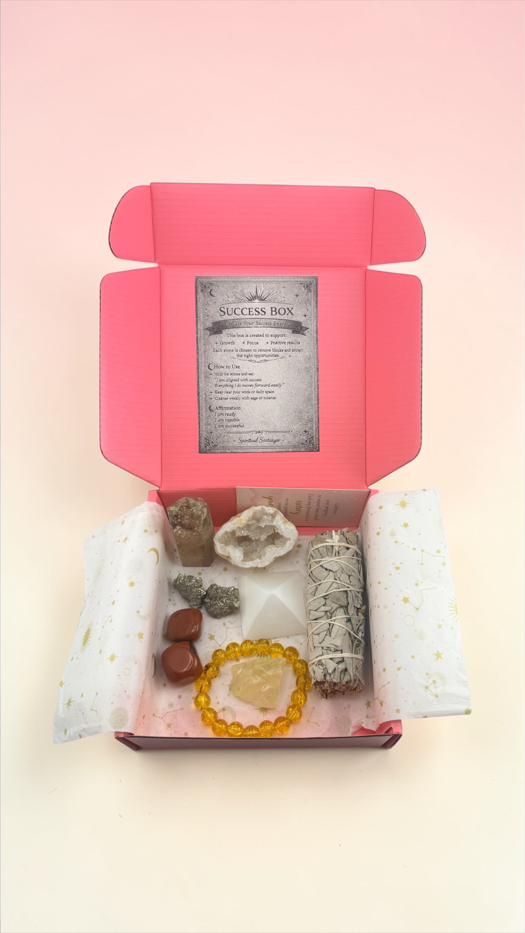 Open pink box containing crystals and a card on a light pink background