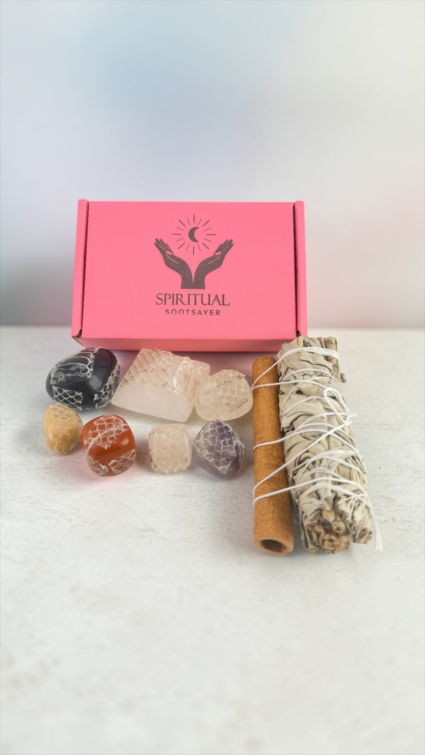 Set of stones, a candle, and a smudge stick in front of a pink box labeled 'Spiritual Initiatives' on a white background.