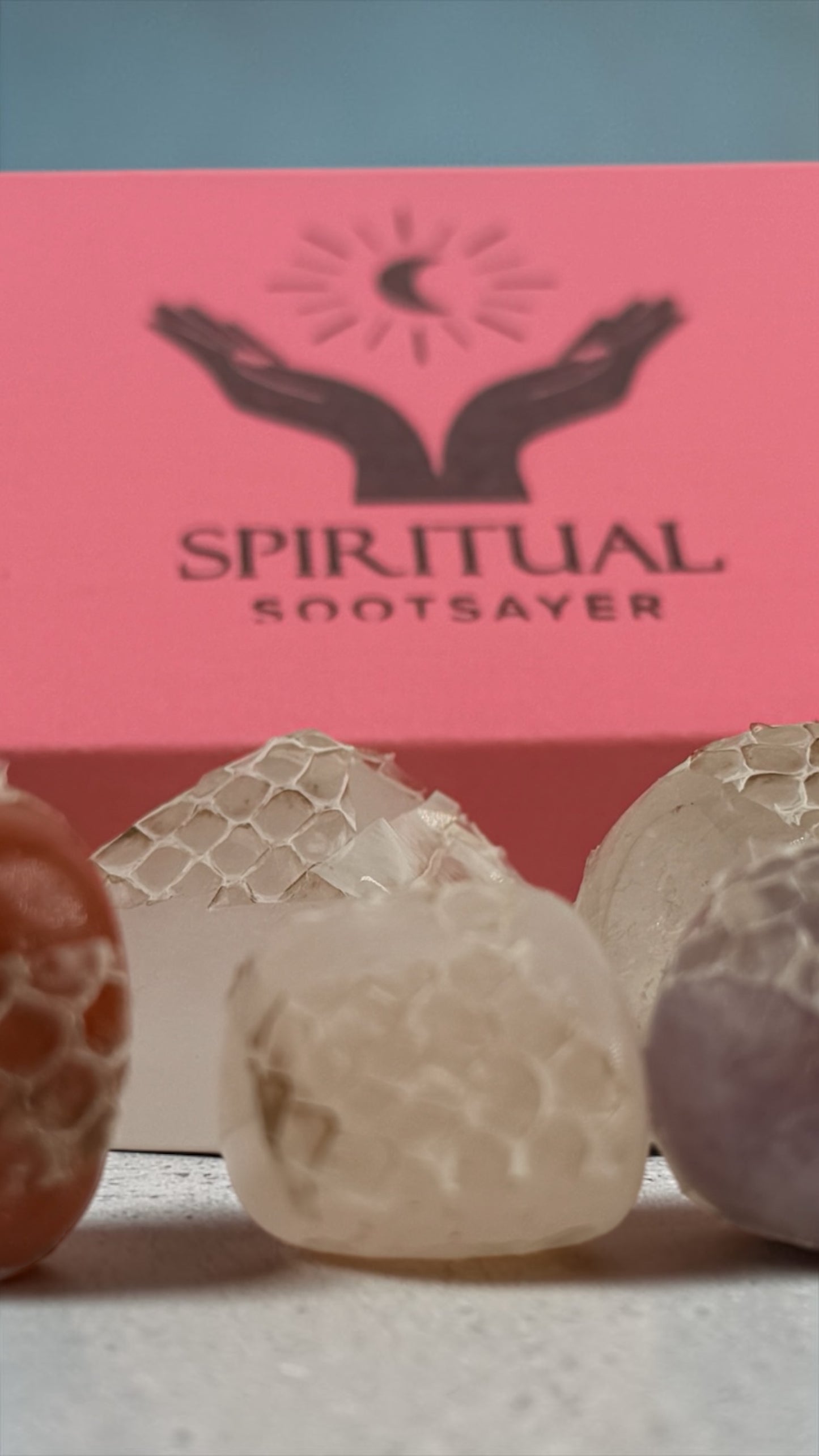 Three soaps with textured surfaces in front of a 'Spiritual Sootsayer' branded box.