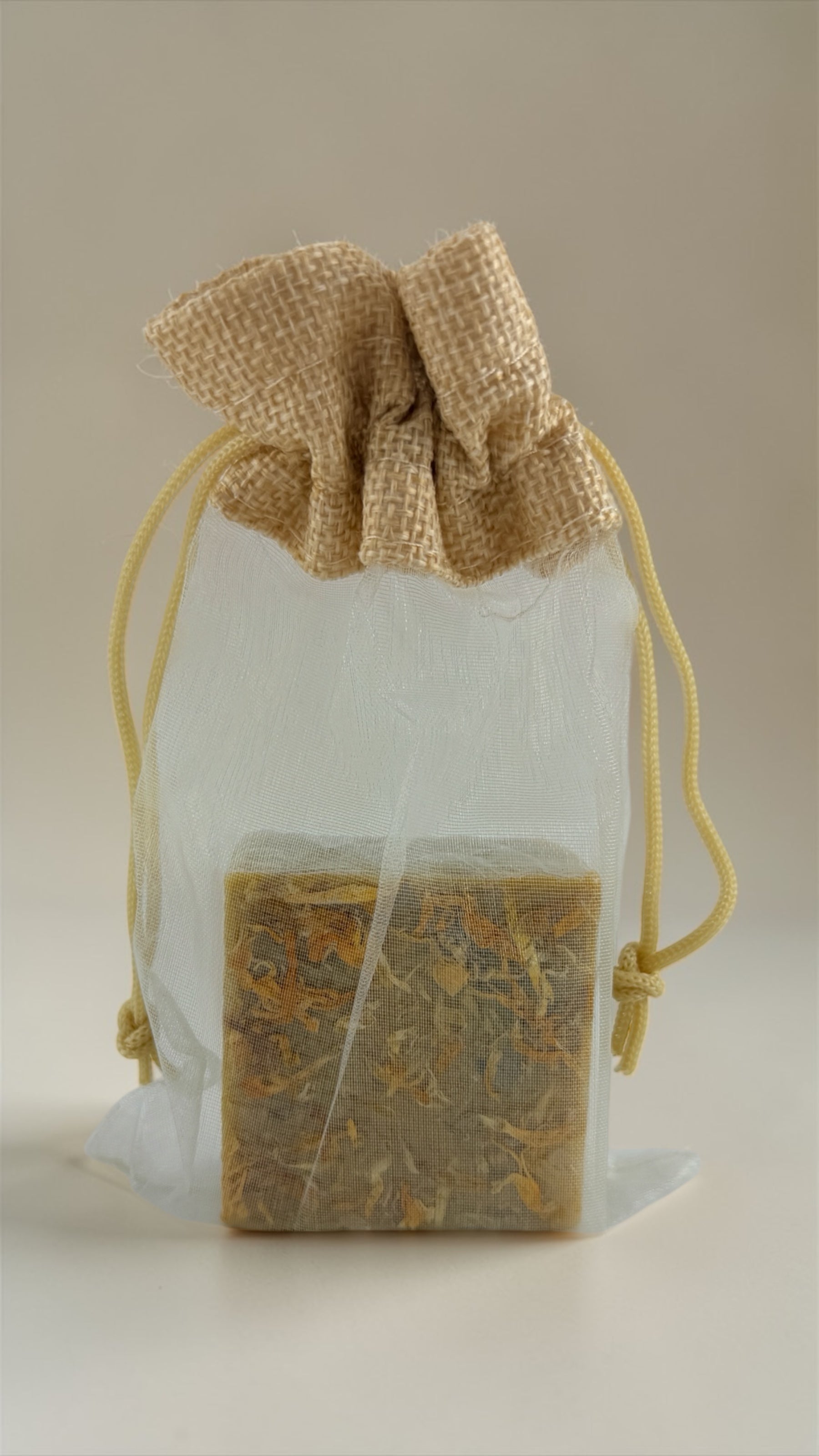 Bar of soap in a clear bag with a burlap drawstring on a beige background