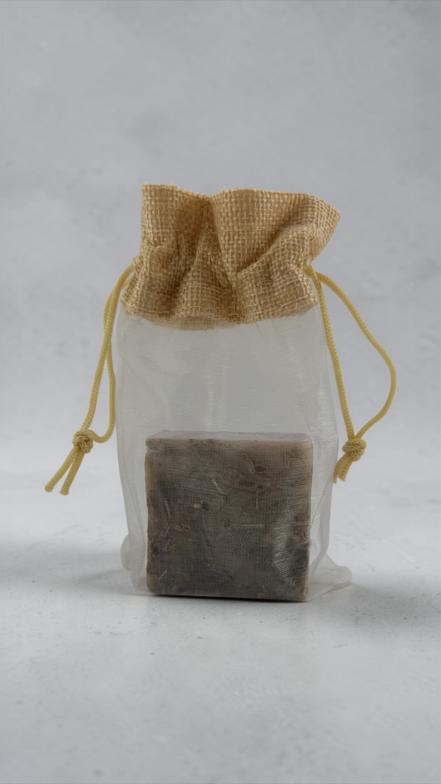 Bar of soap in a clear drawstring bag with a brown drawstring on a light gray background