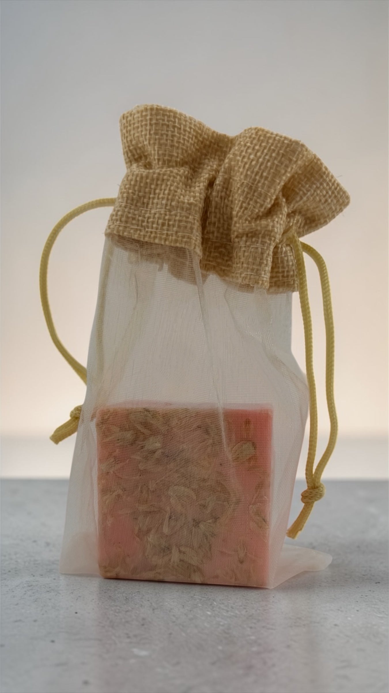 Bar of soap in a clear drawstring bag with burlap top on a light background