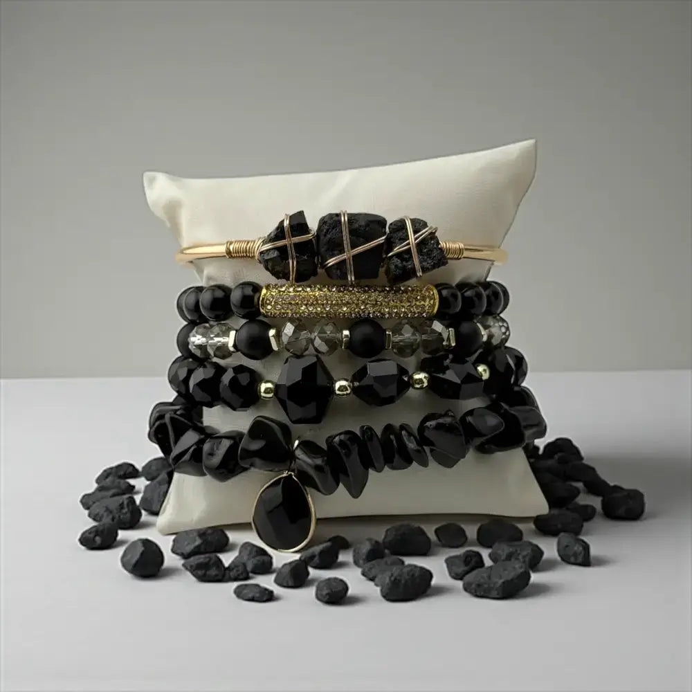 Black beaded bracelets with gold accents on a white pillow against a gray background