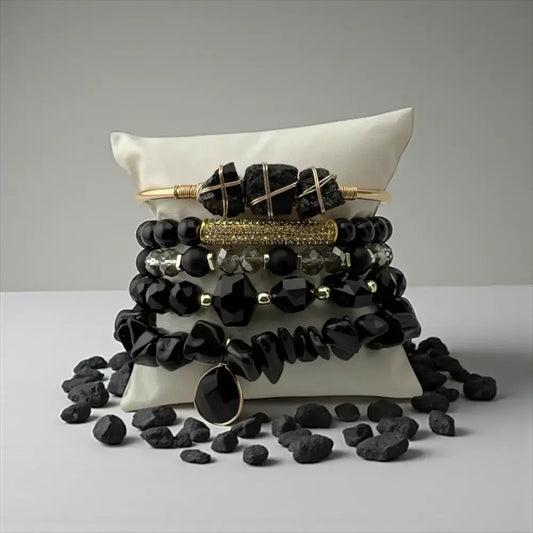 Black beaded bracelets with gold accents on a white pillow against a gray background