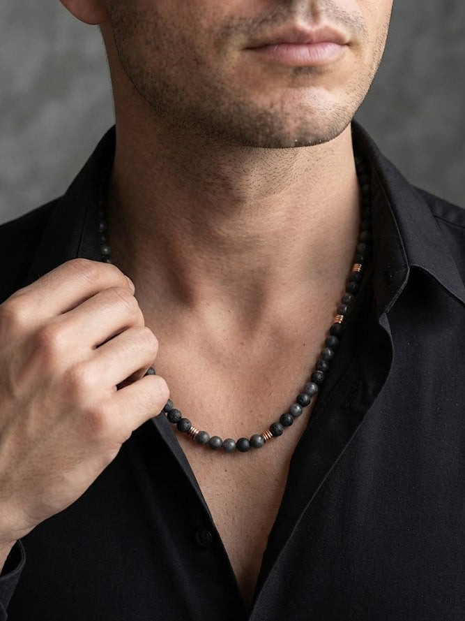 Man wearing a black beaded necklace against a gray background