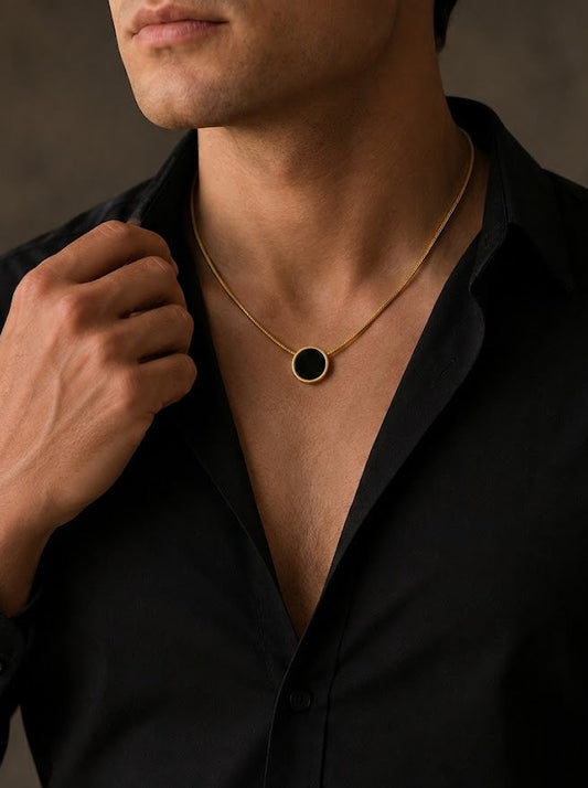 Man wearing a black shirt with a gold necklace featuring a black circle pendant against a neutral background