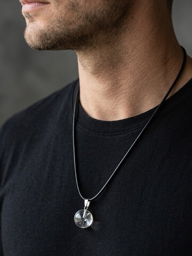 Man wearing a black shirt with a necklace featuring a round pendant.